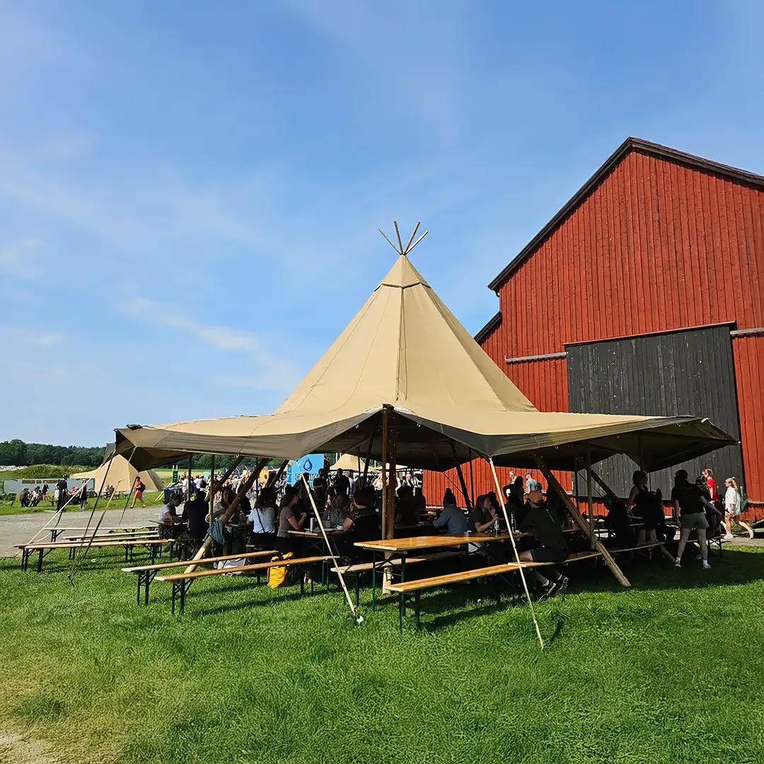 Mennesker ved borde under en åben tipi ved en rød bygning