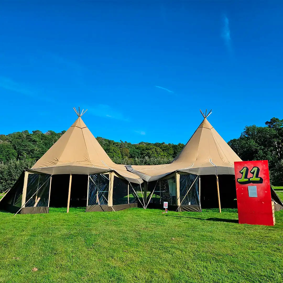To sammenkoblede tipier med transparente sider på en stor, grøn eng. Perfekt løsning til festivaler, teambuilding eller firmaarrangementer
