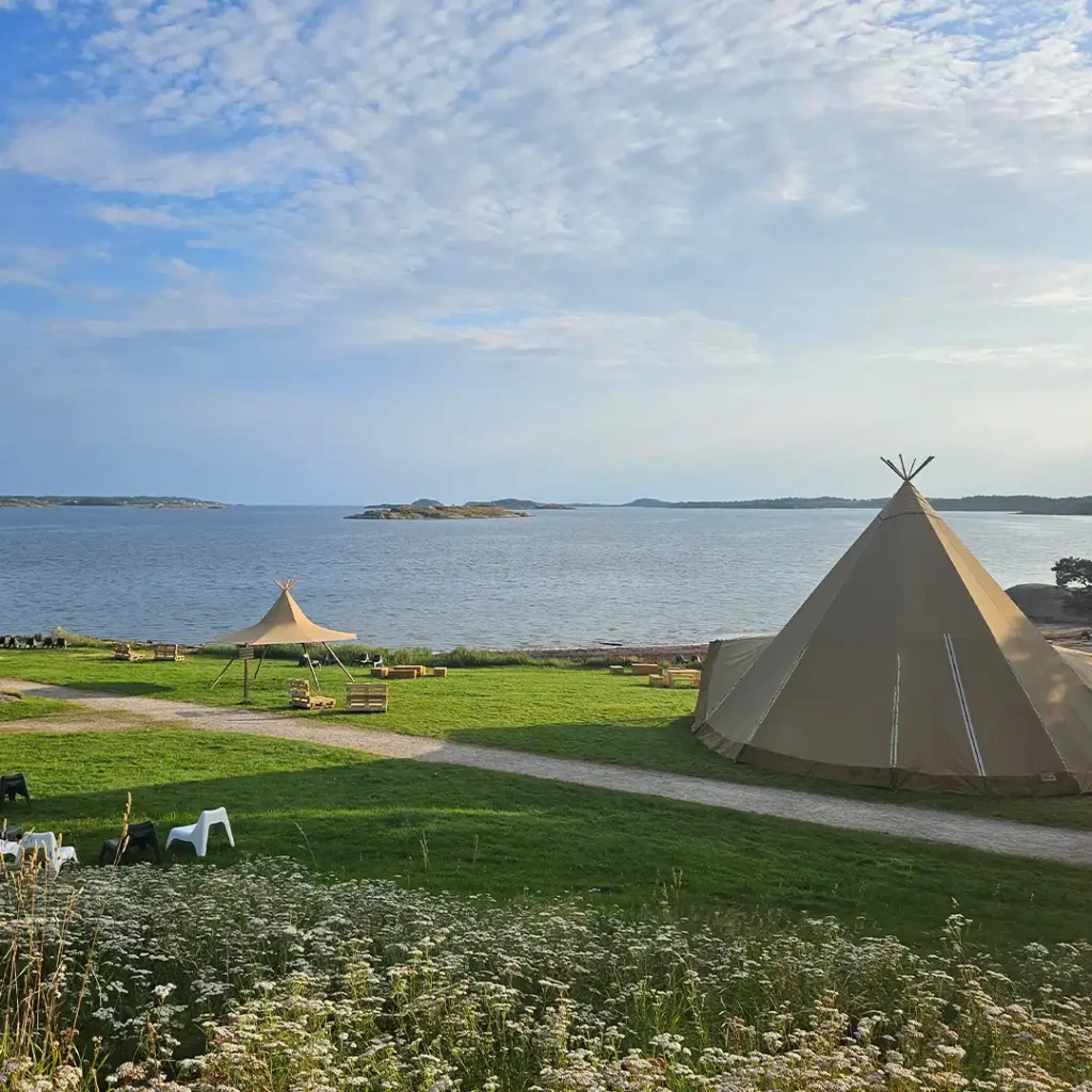 Tipier og et elegant telt placeret ved havet med udsigt over små øer. En idyllisk lokation til bryllupper, retreats og udendørs events.