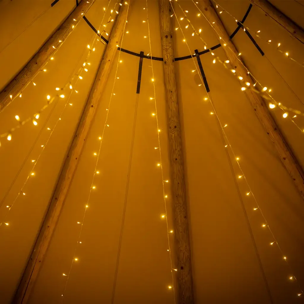 Smukt oplyst tipi-loft med lyskæder, der skaber en varm og hyggelig stemning – perfekt til bryllupper, firmafester og andre begivenheder i telt.