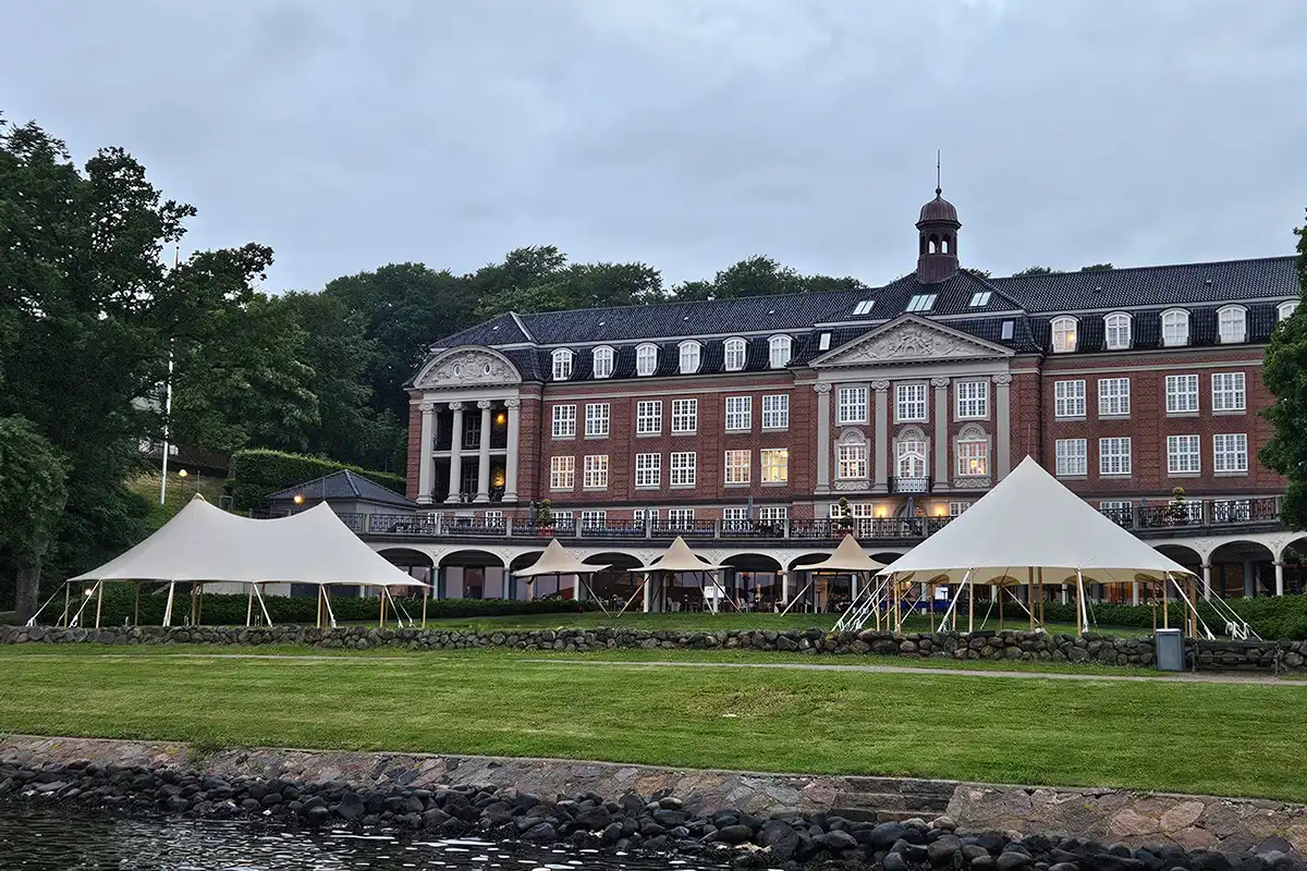 Flere mastetelte opstillet på en grøn plæne foran en storslået, historisk herregård – ideelt til bryllupper, firmaevents, konferencer og eksklusive udendørs arrangementer i elegante omgivelser.