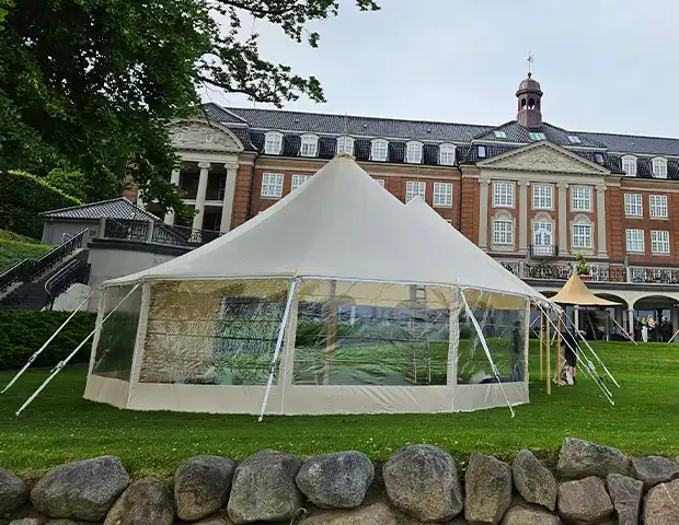 Mastetelt opstillet på en grøn plæne foran en imponerende, historisk bygning – perfekt til bryllupper, firmaevents og eksklusive udendørs arrangementer i klassiske omgivelser.
