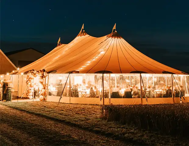 Stort mastetelt oplyst af varme lysdekorationer under en nattefest, fyldt med gæster og festlig stemning – ideelt til bryllupper, jubilæer, firmaevents og udendørs fester med eksklusiv atmosfære.