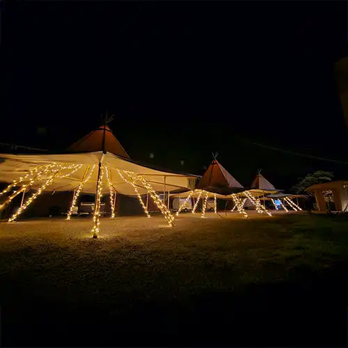 Oplyste tipi-telte i en smuk natteopsætning, ideelt til events, fester og eksklusive sammenkomster i naturskønne omgivelser.