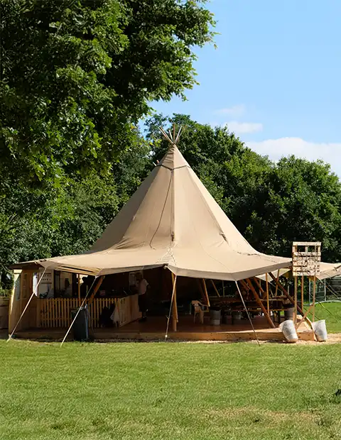 Stort tipi-telt opsat på en grøn eng med rustik bar og hyggelig stemning, perfekt til bryllupper, festivaler og firmaevents – TipiogCo.