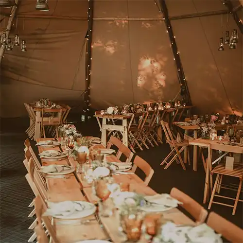 Langbord med blomsterdekoration i en tipi, perfekt til bryllupper og festlige begivenheder.