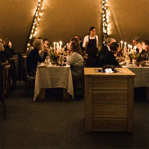 Gæster nyder en hyggelig middag i en tipi, oplyst af levende lys og eventyrlig belysning
