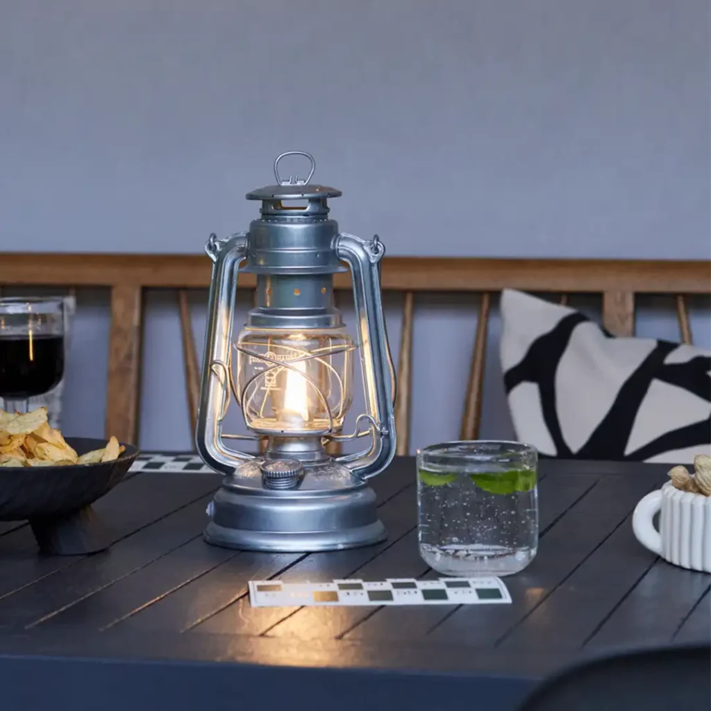 Elegant Petromax lanterne i zink på et bord dækket med snacks og drinks. Perfekt til at skabe en hyggelig atmosfære ved udendørs events, fester eller intime sammenkomster.