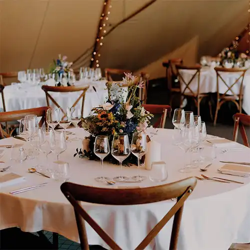 Elegant bordopdækning med blomster og glas på runde borde i en tipi til fest.