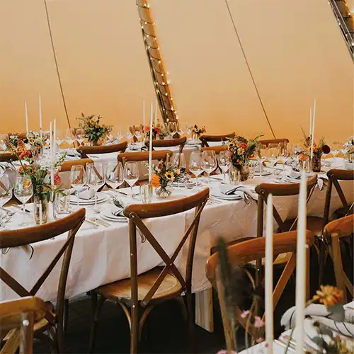 En elegant og rustik bordopstilling i tipi med lange træborde, krydsrygstole og lysestager til en hyggelig middag