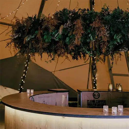 En rund bar i en tipi med elegant belysning og en smuk hængende blomsterdekoration, perfekt til fester og events