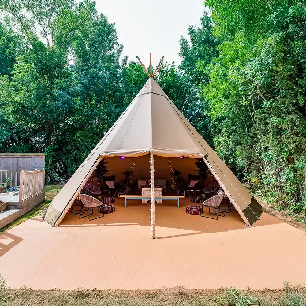 En smukt indrettet tipi-lounge med komfortable stole, puder og dekorative lyskæder, omgivet af grønne træer. Perfekt til afslapning, eksklusive events eller glamping-oplevelser.