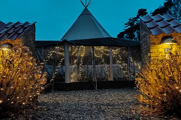 Stemningsfuldt tipi-telt med lyskæder, opsat i en charmerende gårdhave, perfekt til intime bryllupper, firmafester og eksklusive events – TipiogCo.