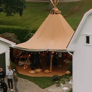 Indvendigt billede af Stratus 40 tipi med træborde, blomster og lamper, klar til bryllup eller middag.